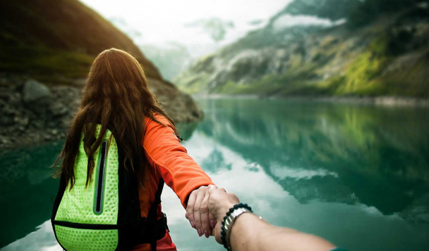 People holding hands and looking out toward a glacier lake with mountains surrounding it