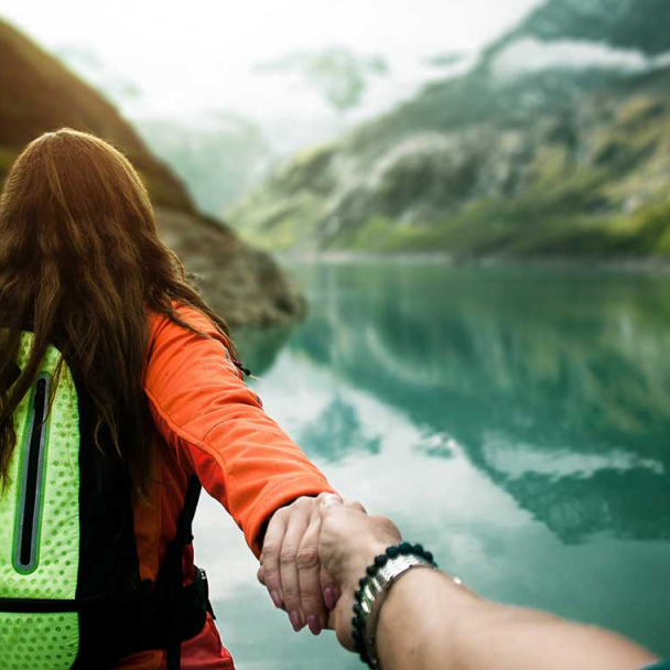 People holding hands and looking out toward a glacier lake with mountains surrounding it